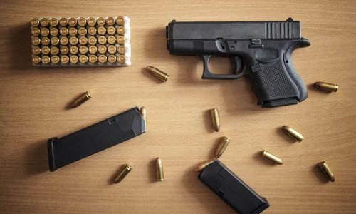 Gun with box of ammunition and bullets on wooden background.
