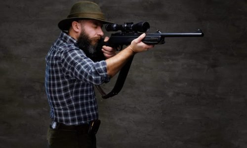 Hunter aiming a rifle in sight while preparing to make an accurate shot at the prey. Isolated on a dark background.